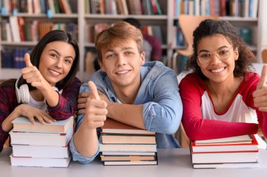 Kütüphanede baş parmak hareketi gösteren genç öğrenciler