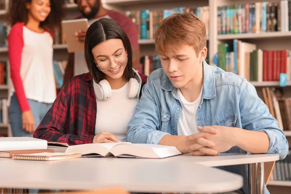 Jovens estudantes lendo livro enquanto se preparam para o exame na biblioteca — Fotografia de Stock