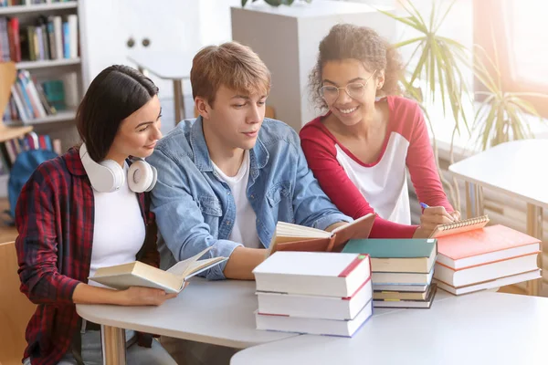 Jovens estudantes lendo livros enquanto se preparam para o exame na biblioteca — Fotografia de Stock