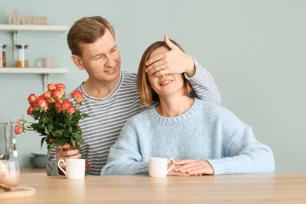 Happy husband giving his wife bouquet of flowers in kitchen at home — Stock Photo, Image