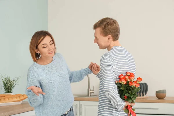 Счастливый муж с букетом цветов для жены на кухне дома — стоковое фото