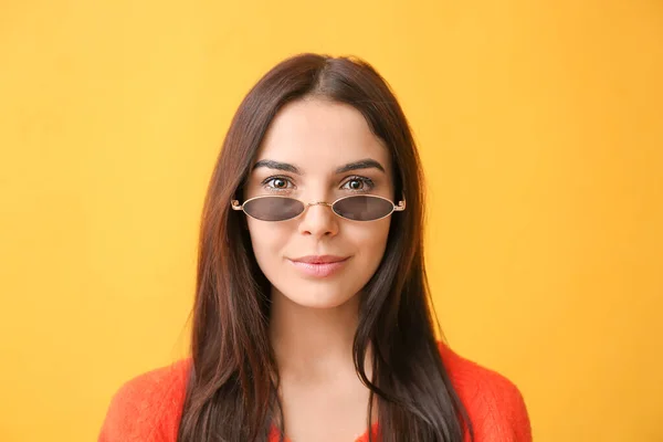 Jovem mulher com óculos de sol elegantes no fundo de cor — Fotografia de Stock