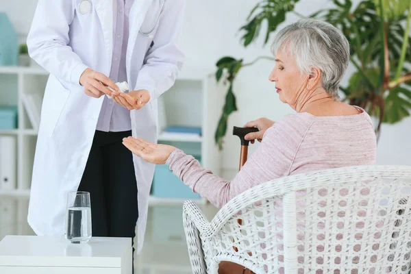 Жінка-лікар дає старшій жінці, яка страждає від синдрому Паркінсона таблетки в клініці — стокове фото
