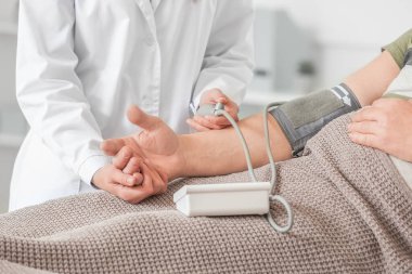 Klinikte Parkinson sendromu olan yaşlı bir adamın tansiyonunu ölçen kadın doktor.