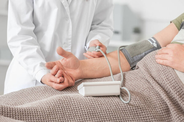 Female doctor measuring blood pressure of senior man suffering from Parkinson syndrome in clinic