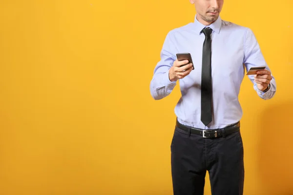 Male bank manager with credit card and mobile phone on color background — Stock Photo, Image