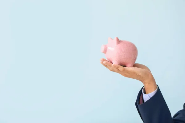 Hand of bank manager with piggy bank on light background