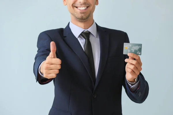 Male bank manager with credit card showing thumb-up gesture on light background — Stock Photo, Image