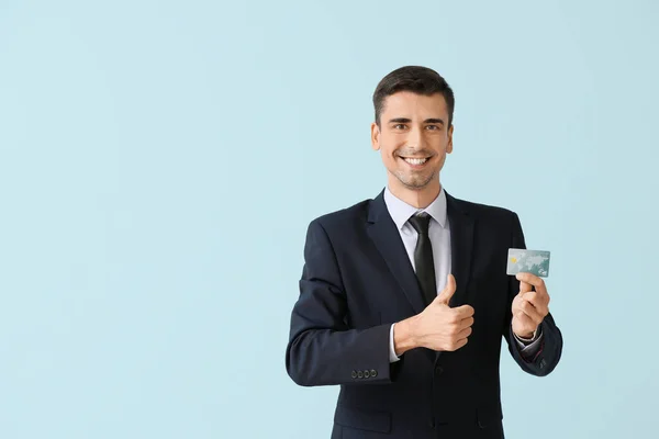 Male bank manager with credit card showing thumb-up gesture on light background — Stock Photo, Image