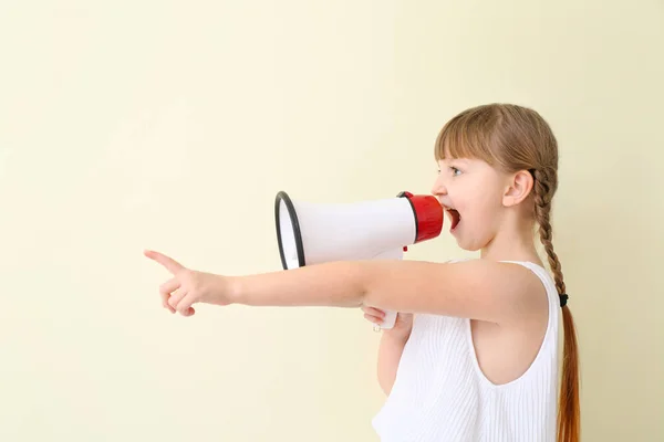 Cute little girl with megaphone pointing at something on light background — Stock Photo, Image