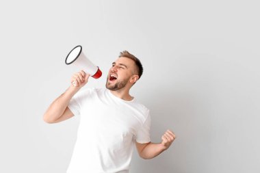 Emotional young man with megaphone on light background clipart