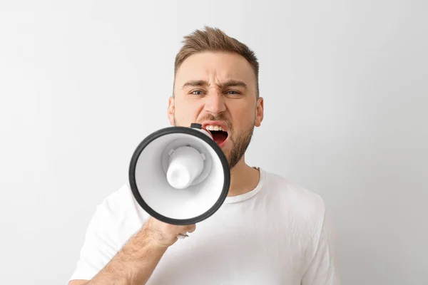 Emotional young man with megaphone on light background — Stock Photo, Image