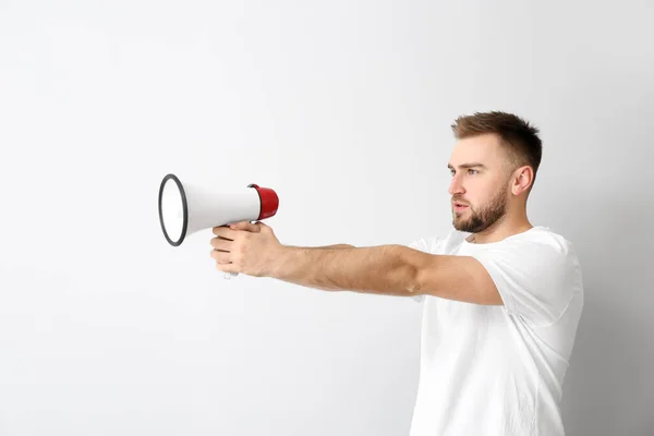 Emotional young man with megaphone on light background — Stock Photo, Image