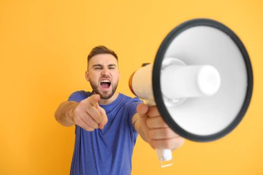 Emotional young man with megaphone on color background clipart