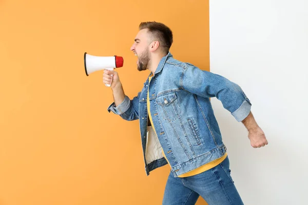 Emotional young man with megaphone on color background — Stock Photo, Image