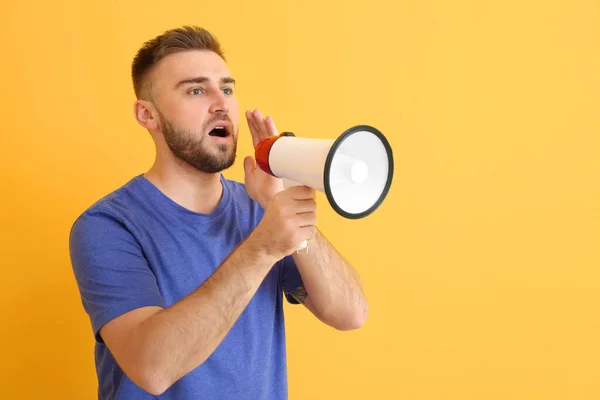 Emotional young man with megaphone on color background — Stock Photo, Image