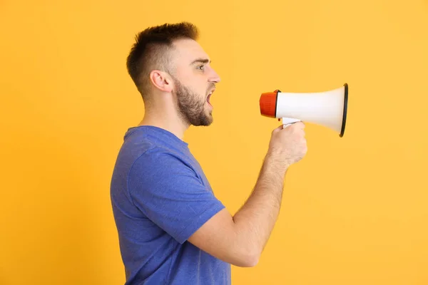 Emotionele jongeman met megafoon op kleur achtergrond — Stockfoto