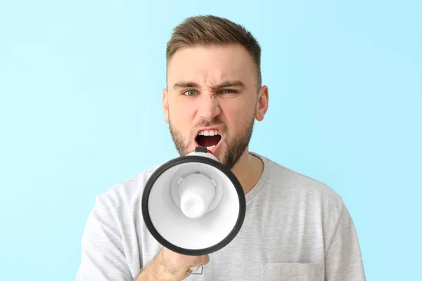 Emotional young man with megaphone on color background — Stock Photo, Image