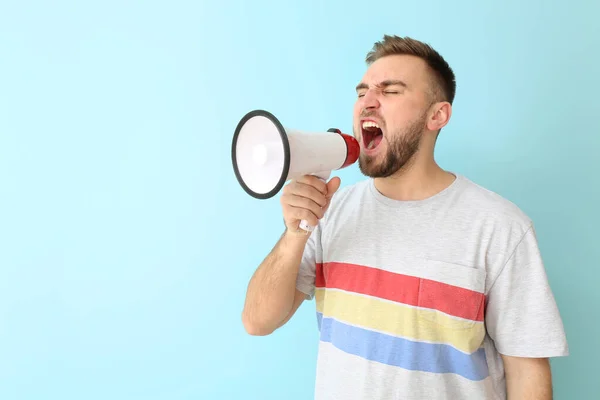 Emotional young man with megaphone on color background — Stock Photo, Image