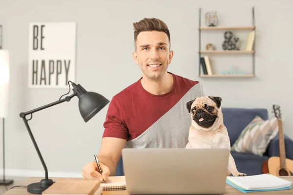 Hombre guapo con lindo perro pug y portátil en casa —  Fotos de Stock