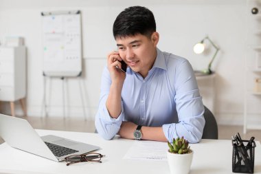 Young Asian businessman talking by phone in office