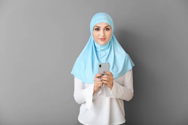 Gri arka planda cep telefonu olan güzel bir Arap kadın.