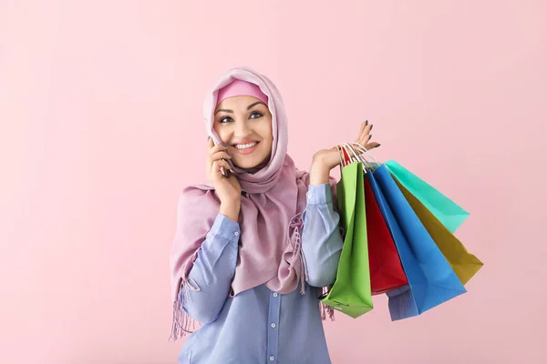 Mujer árabe hermosa con bolsas de compras hablando por teléfono móvil en el fondo de color —  Fotos de Stock