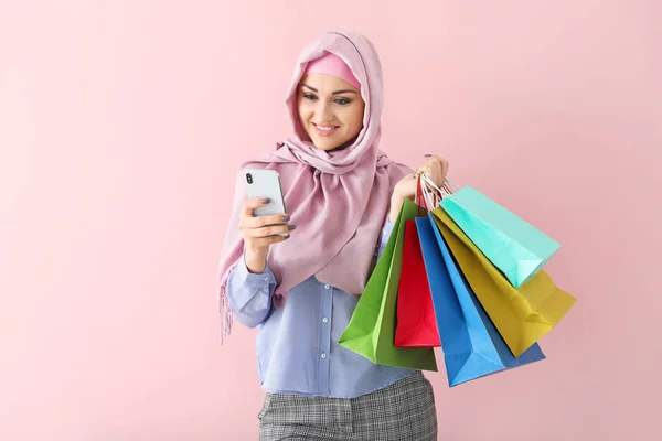 Beautiful Arab woman with mobile phone and shopping bags on color background