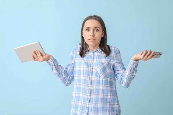 Hilflose Frau mit Tablet-Computer und Handy auf farbigem Hintergrund — Stockfoto