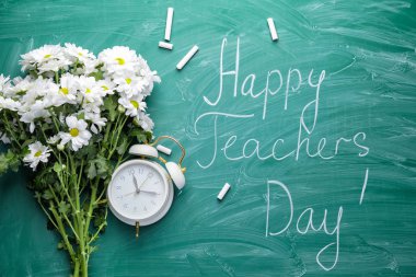 Bir buket çiçek, tebeşir, saat ve mesaj tahtasında Mutlu Öğretmenler Günü.