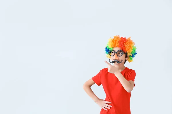 Little boy in funny disguise showing something on light background. April fools' day celebration — Stock Photo, Image
