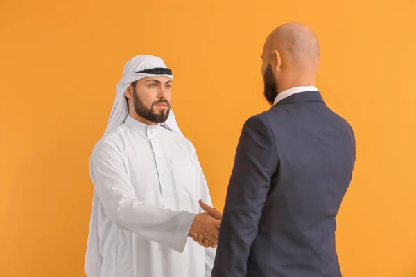 Arab człowiek i jego partner biznesowy uścisk dłoni na tle koloru — Zdjęcie stockowe