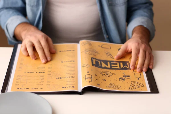 Молодой человек с меню сидит в ресторане — стоковое фото