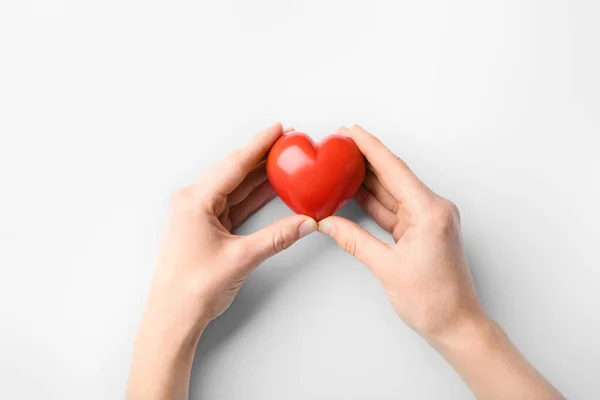มือผู้หญิงที่มีหัวใจสีแดงบนพื้นหลังสีขาว แนวคิดเกี่ยวกับโรคหัวใจ — ภาพถ่ายสต็อก