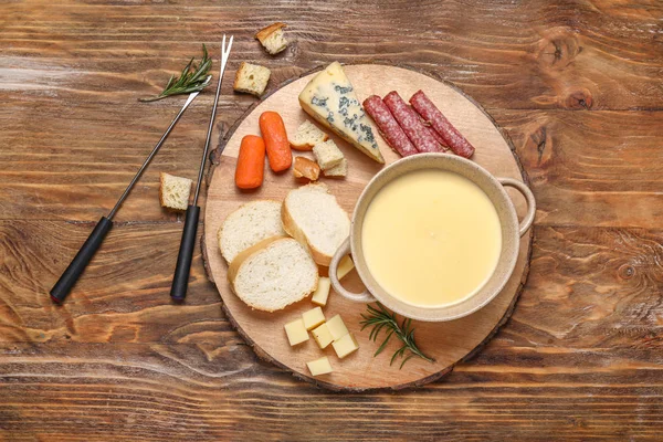 Cheese fondue with snacks on wooden background