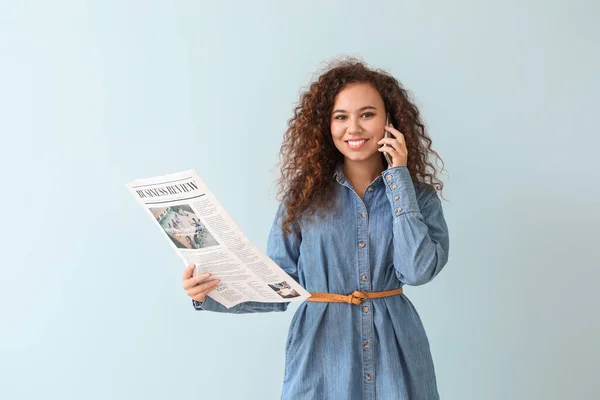 Молода афро-американська жінка з газетою говорить по телефону на кольоровому фоні — стокове фото
