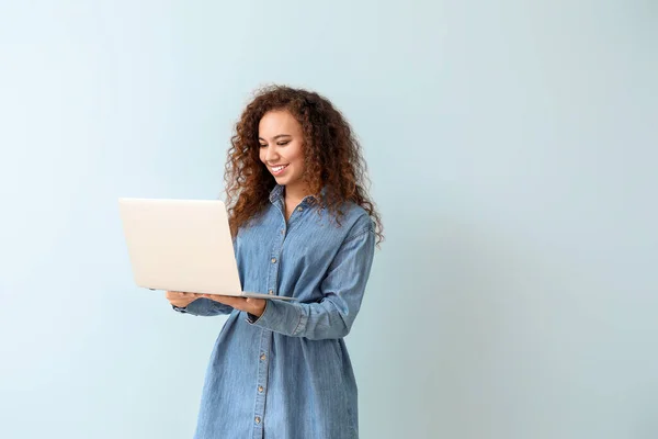 Junge afroamerikanische Frau mit Laptop auf farbigem Hintergrund — Stockfoto