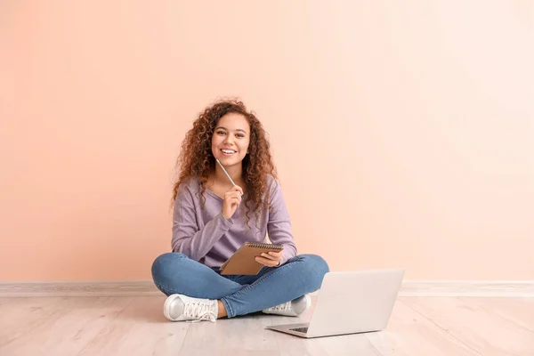 Young African-American woman with laptop sitting near color wall — Stock Photo, Image