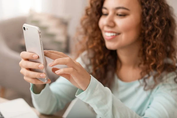 Young African-American woman with mobile phone at home — Stock Photo, Image