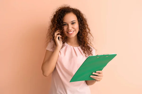 Junge afroamerikanische Geschäftsfrau mit Dokumenten im Telefongespräch auf farbigem Hintergrund — Stockfoto