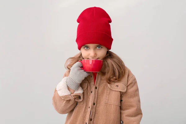 Cute little girl in winter clothes and with cup of hot chocolate on light background — Stock Photo, Image