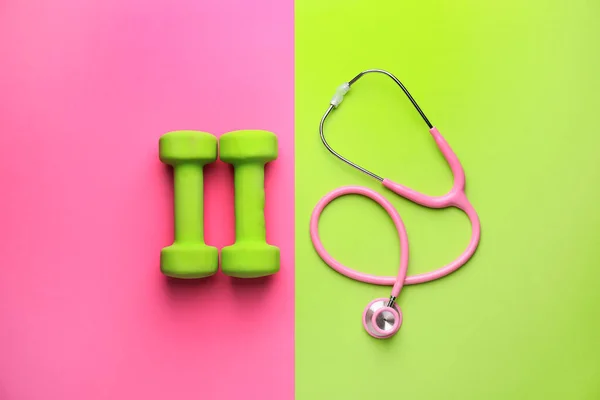 Stethoscope and dumbbells on color background — Stock Photo, Image