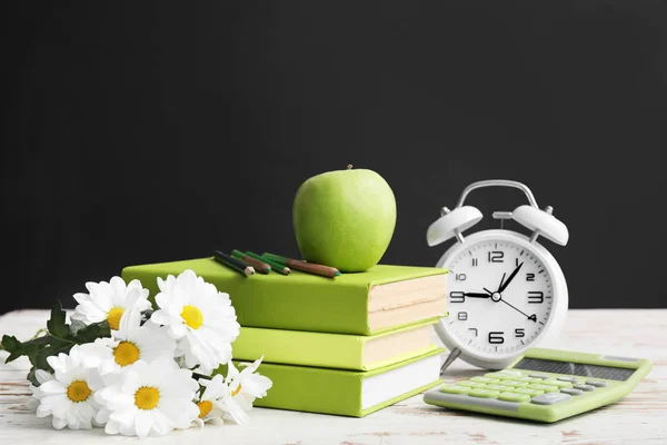 School stationery, apple, flowers and clock on table in classroom. Teacher\'s Day celebration