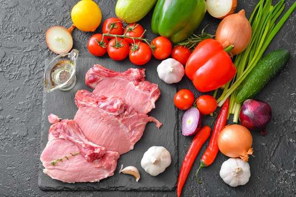 Carne de cerdo cruda con verduras y aceite sobre fondo oscuro — Foto de Stock