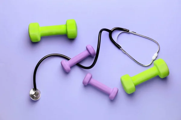 Stethoscope and dumbbells on color background — Stock Photo, Image