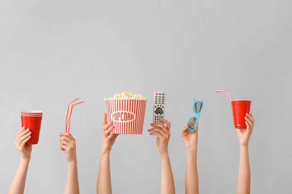 Many hands with popcorn, drink, remote control and eyeglasses on grey background