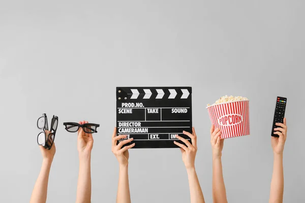 Many hands with popcorn, remote control, movie clapper and eyeglasses on grey background