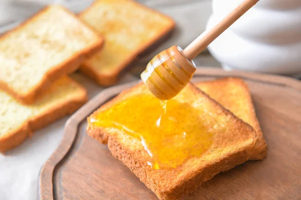 Madu manis menetes di atas roti panggang di atas meja — Stok Foto