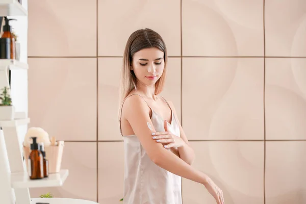 Gyönyörű fiatal nő alkalmazása krém a karján a fürdőszobában — Stock Fotó