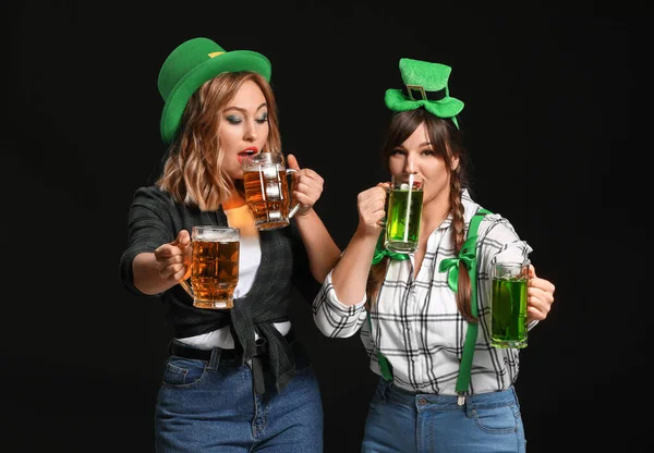 Funny young women with beer on dark background. St. Patrick\'s Day celebration